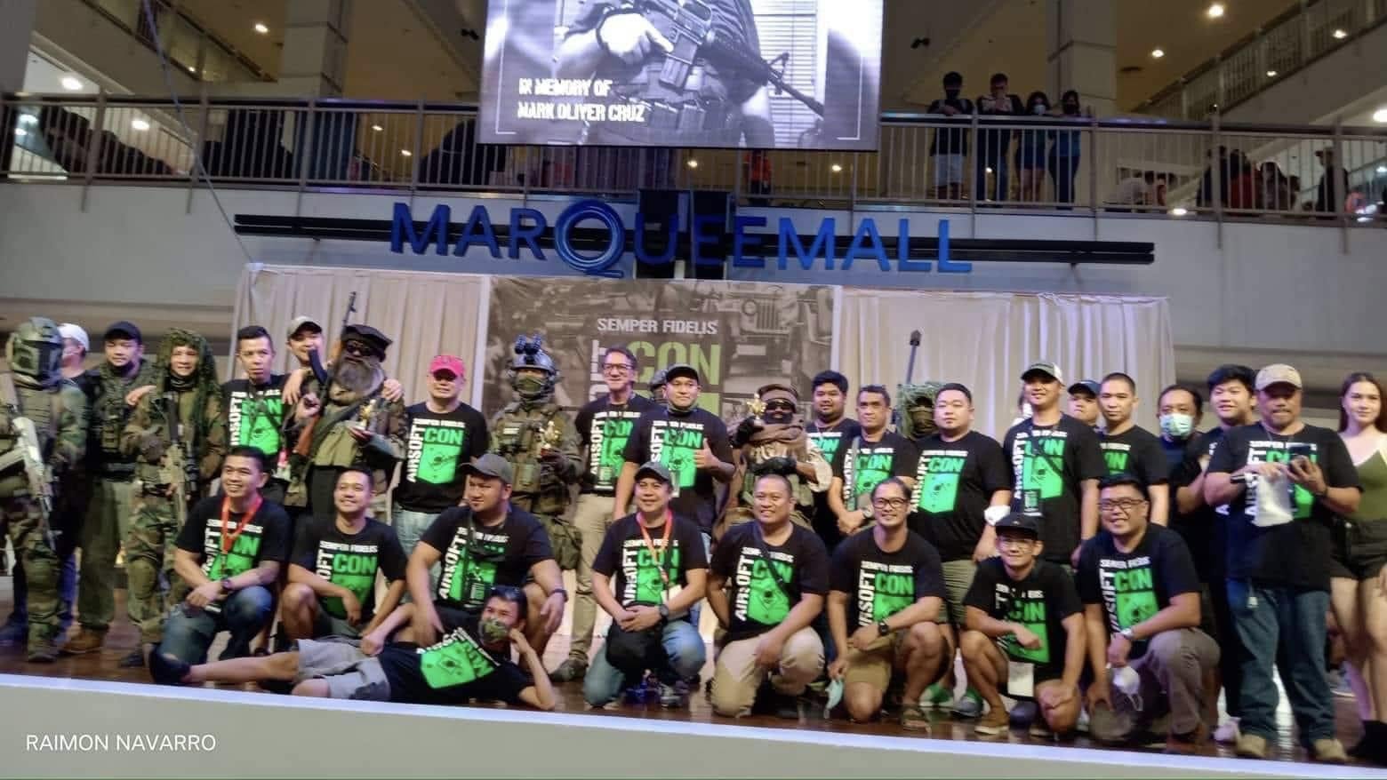 The team gathers at the Semper Fidelis Airsoft Con display in Marquee Mall, with a tribute to Mark Oliver Cruz shown behind them.