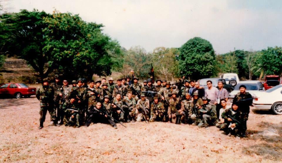 An early team photograph taken in an open field, parked cars in the background.
