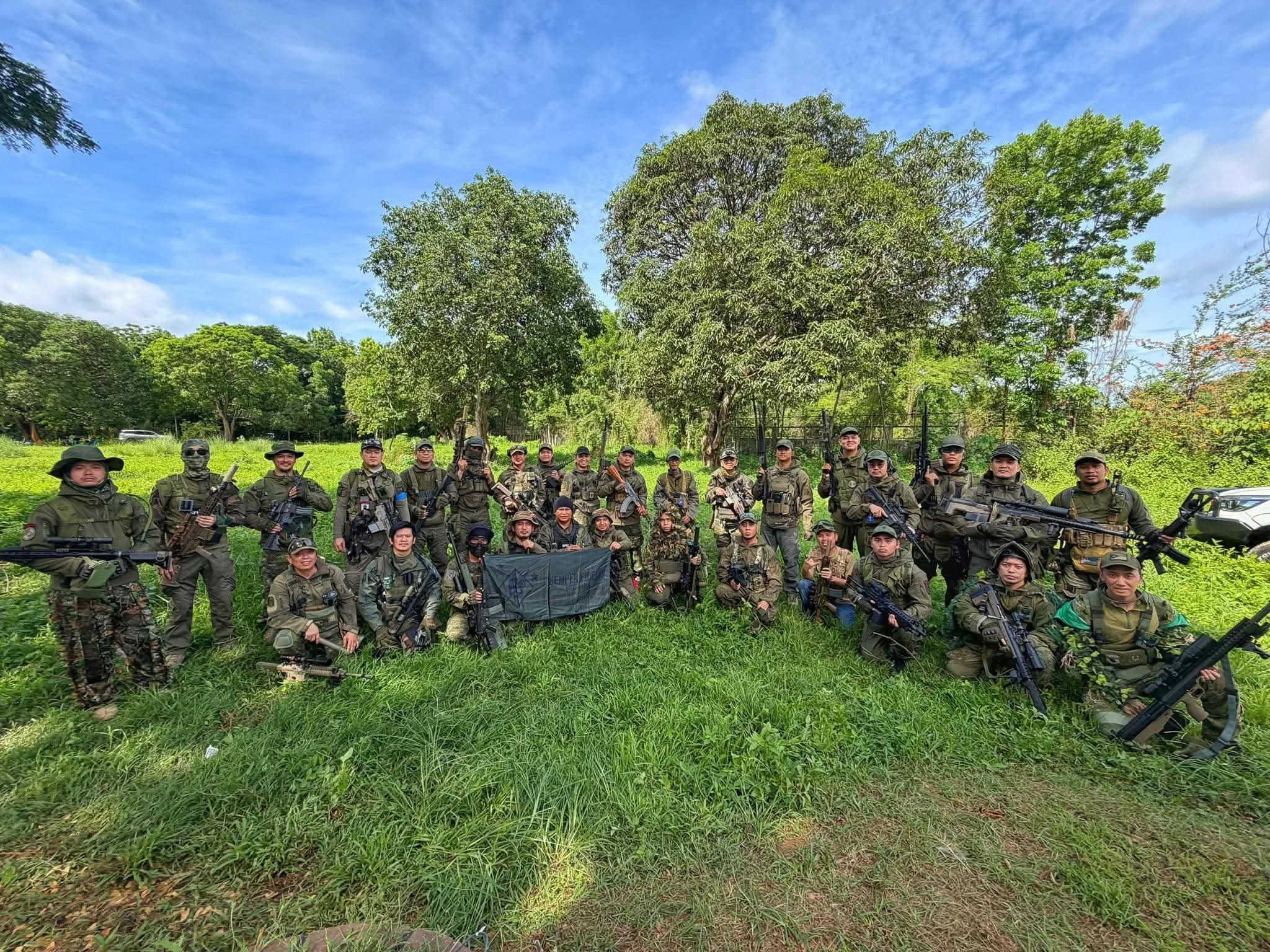 The roster gathers in an open field beneath a clear sky, team banner in hand.