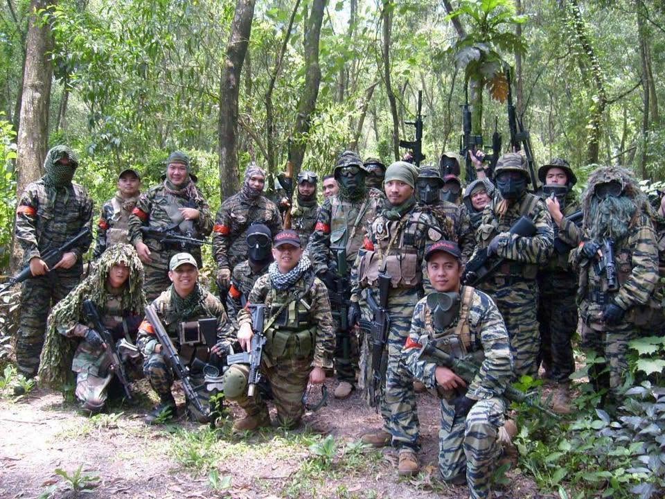 A squad in tiger-stripe camouflage and red armbands poses in the forest.